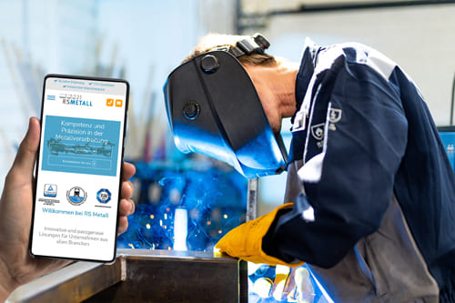Schweißen in der Metallverarbeitung mit mobiler Webseite von RS Metall im Vordergrund Schweißer bei der Arbeit mit Schutzmaske, daneben ein Smartphone mit einer Metallverarbeitungs-Webseite von Rudi Schindhelm Metall GmbH & Co KG